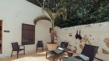 Un patio con dos sillones, una palmera en maceta y una pared con pintura descascarada.