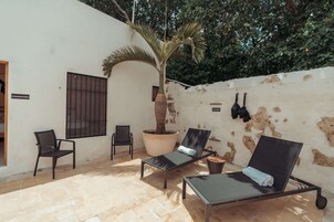 Un patio con dos sillones, una palmera en maceta y una pared con pintura descascarada.