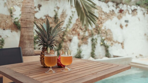 Una mesa de madera con dos vasos de una bebida ámbar y una piña.