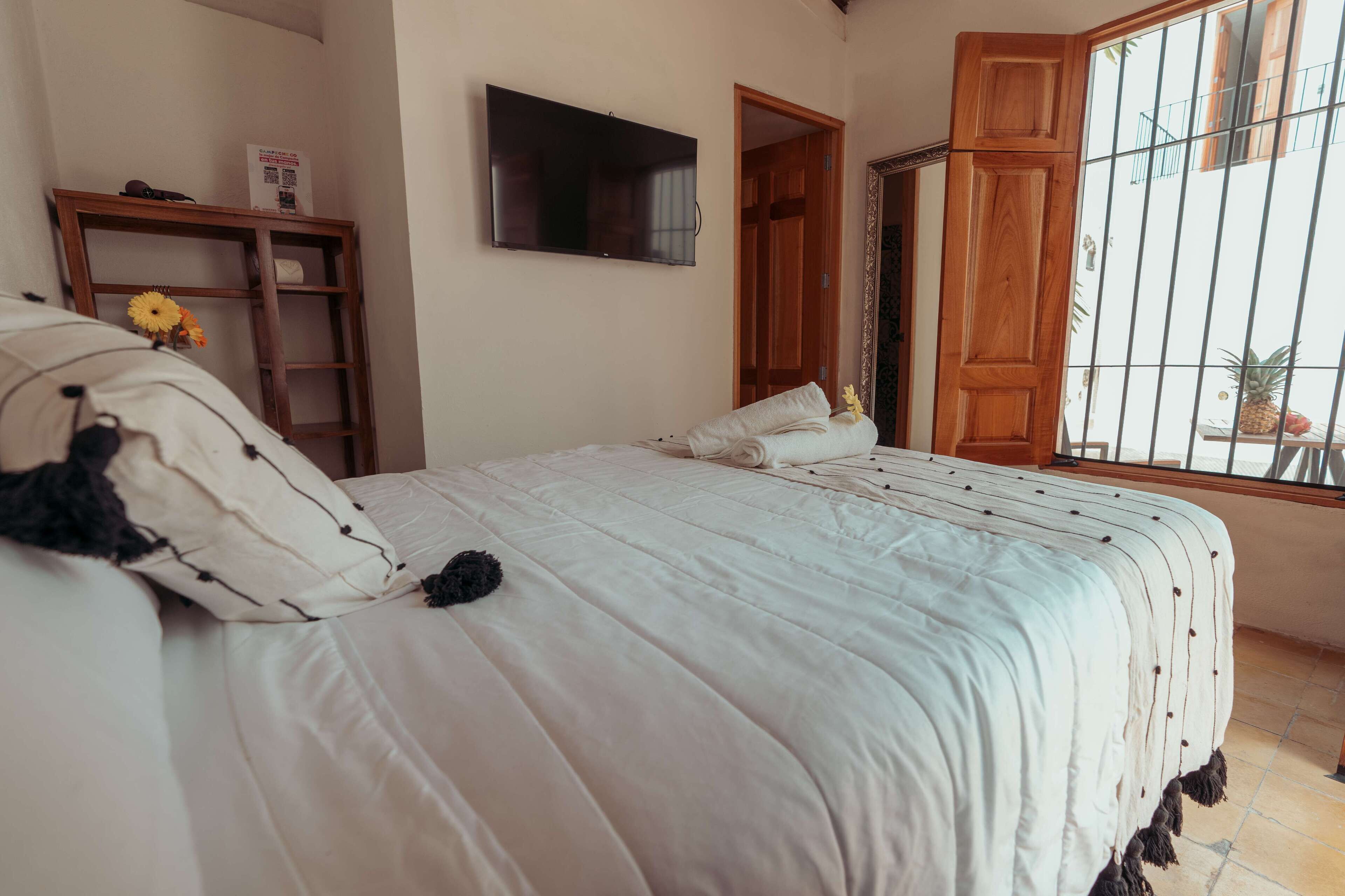 A bedroom with a bed, a TV, a wooden wardrobe, and a window with bars.