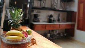Una encimera de cocina con un frutero que contiene plátanos, una piña y un pitahaya.