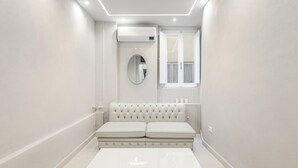 A modern bathroom with a white bathtub, a cushioned bench, a round mirror, and a window with curtains. - Live the Heart of Florence: Design Suite 30m from Ponte Vecchio and Pitti Palace (Firenze)