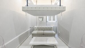 A narrow, modern bathroom with a white vanity, a tufted bench, and a hanging light fixture. - Live the Heart of Florence: Design Suite 30m from Ponte Vecchio and Pitti Palace (Firenze)