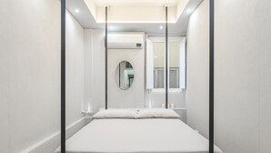 A modern, minimalist bedroom with a large bed, a round mirror, and a window with white shutters. - Live the Heart of Florence: Design Suite 30m from Ponte Vecchio and Pitti Palace (Firenze)