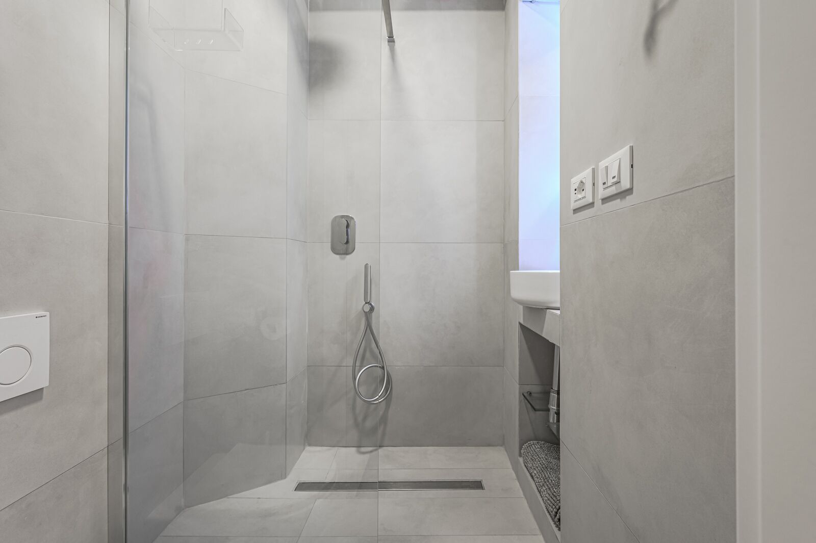 A modern shower with a glass door, a handheld showerhead, and a control panel on the wall.