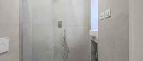 A modern shower with a glass door, a handheld showerhead, and a control panel on the wall.