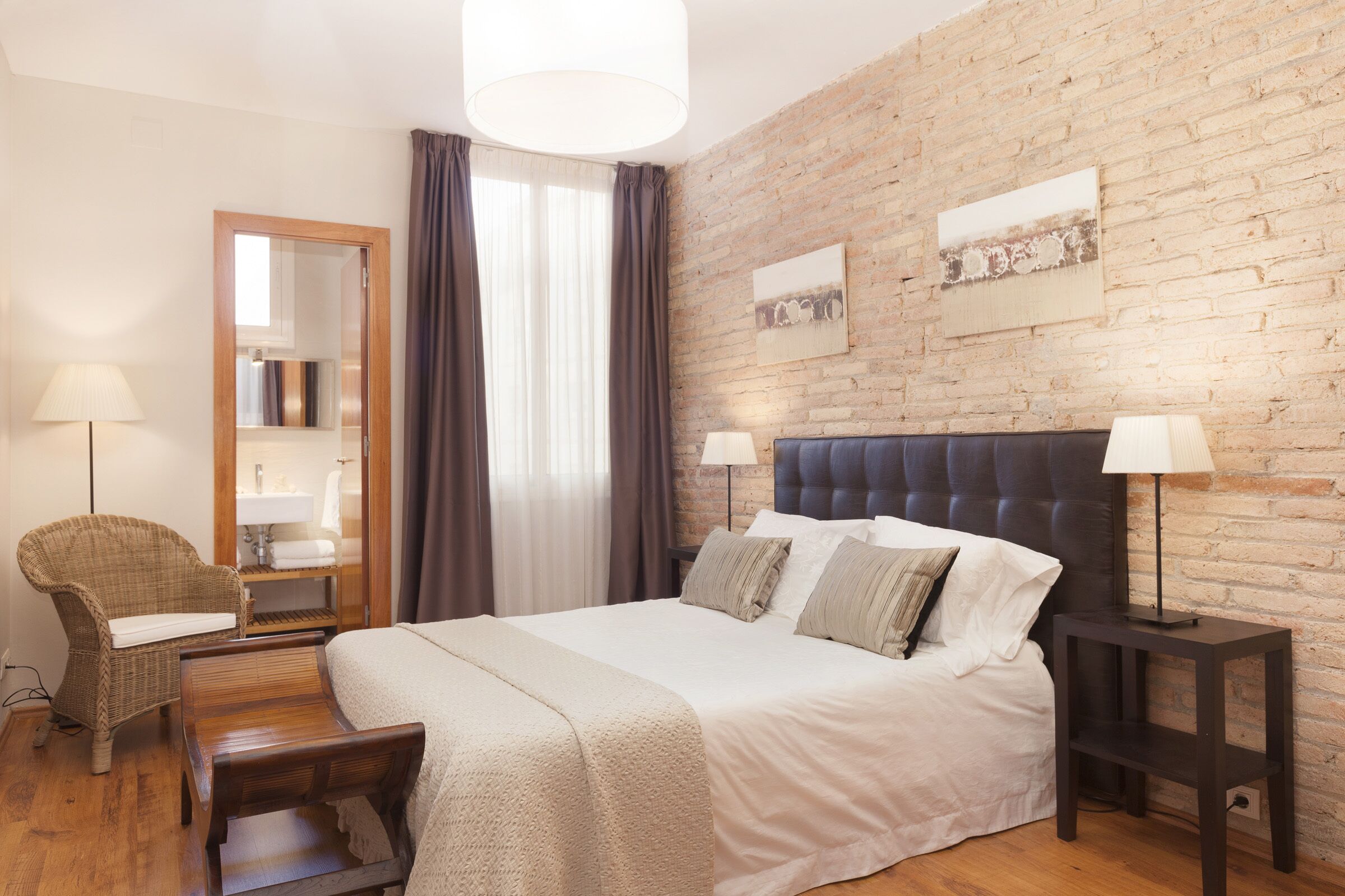 Un dormitorio con una cama grande, una mesita de noche de madera, una silla, un espejo y una pared de ladrillo.