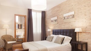 A bedroom with a large bed, a wooden nightstand, a chair, a mirror, and a brick wall. - Sant Pau 5 - Superb 3-bedroom apartment in central Barcelona (Barcelona)