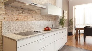 A modern kitchen with a granite countertop, white cabinetry, a brick accent wall, and a stainless steel range hood. - Sant Pau 5 - Superb 3-bedroom apartment in central Barcelona (Barcelona)