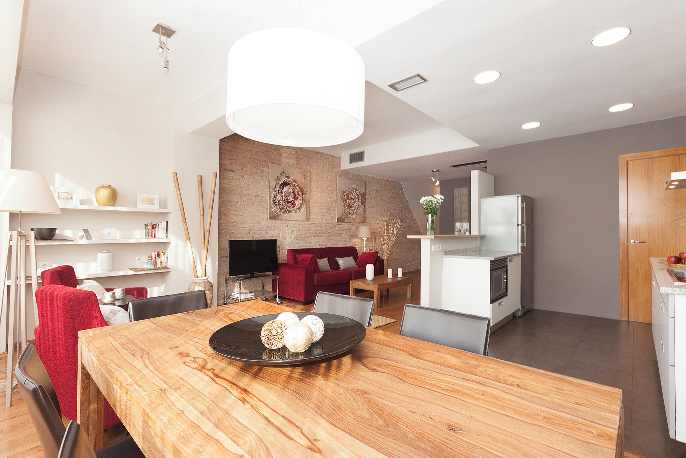 Una sala de estar moderna con comedor, que incluye una mesa de madera, sofá rojo y una cocina al fondo.