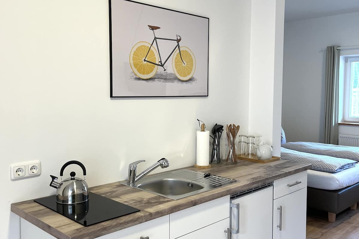 Eine moderne Küche mit einem Edelstahlkocher, einer Spüle und einer Arbeitsplatte. An der Wand hängt ein gerahmtes Bild von einem Fahrrad.