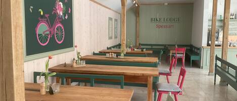A restaurant with wooden tables and chairs, a chalkboard with a bicycle illustration, and a sign reading "BIKE LODGE Spessart".