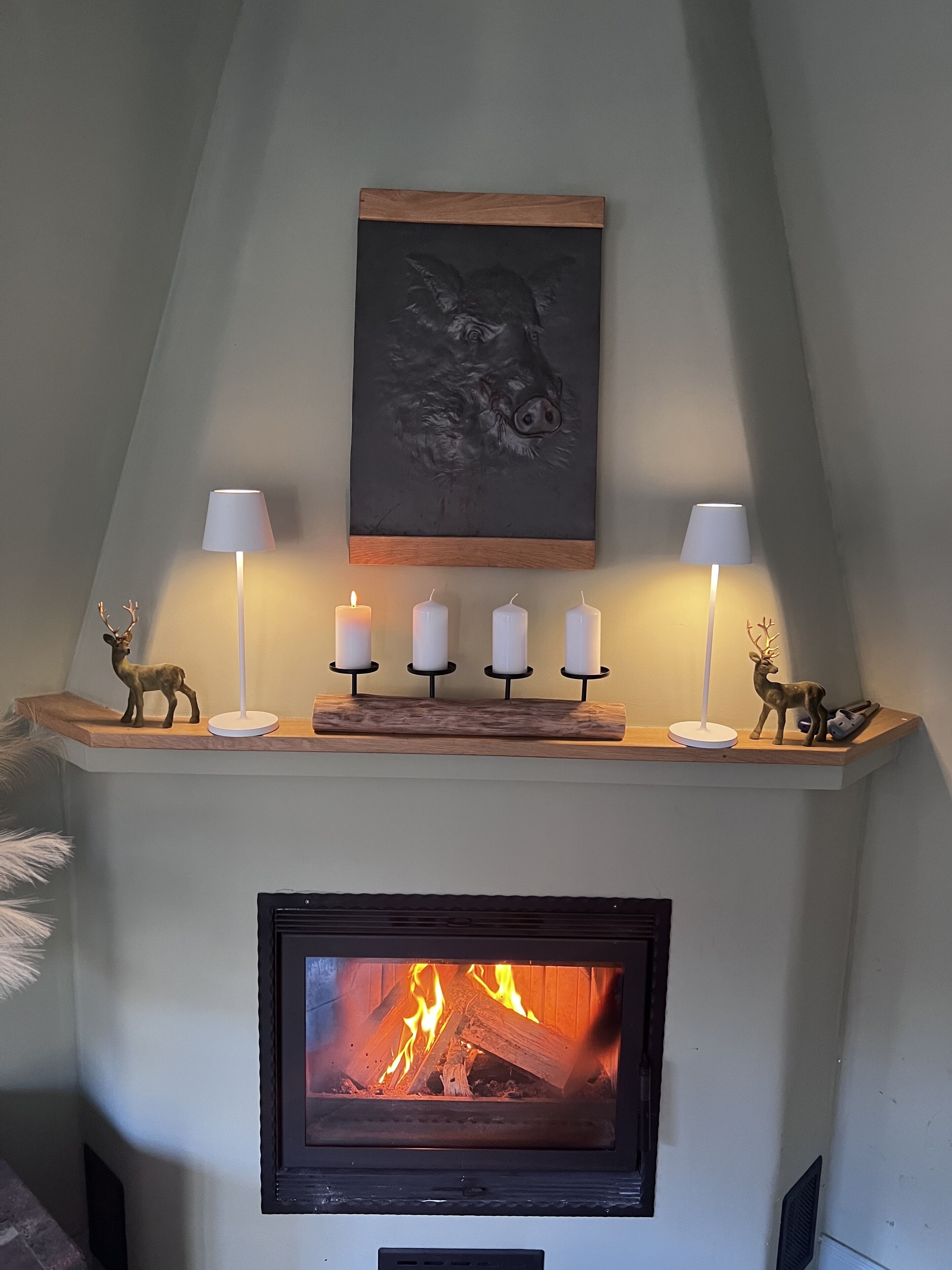 Una chimenea con un repisa mostrando una figurita de ciervo, una escultura de cerdo y cuatro velas encendidas.