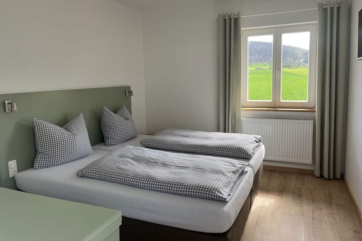 Ein Schlafzimmer mit zwei Betten, einem Heizkörper und einem Fenster mit Blick auf eine grüne Landschaft.
