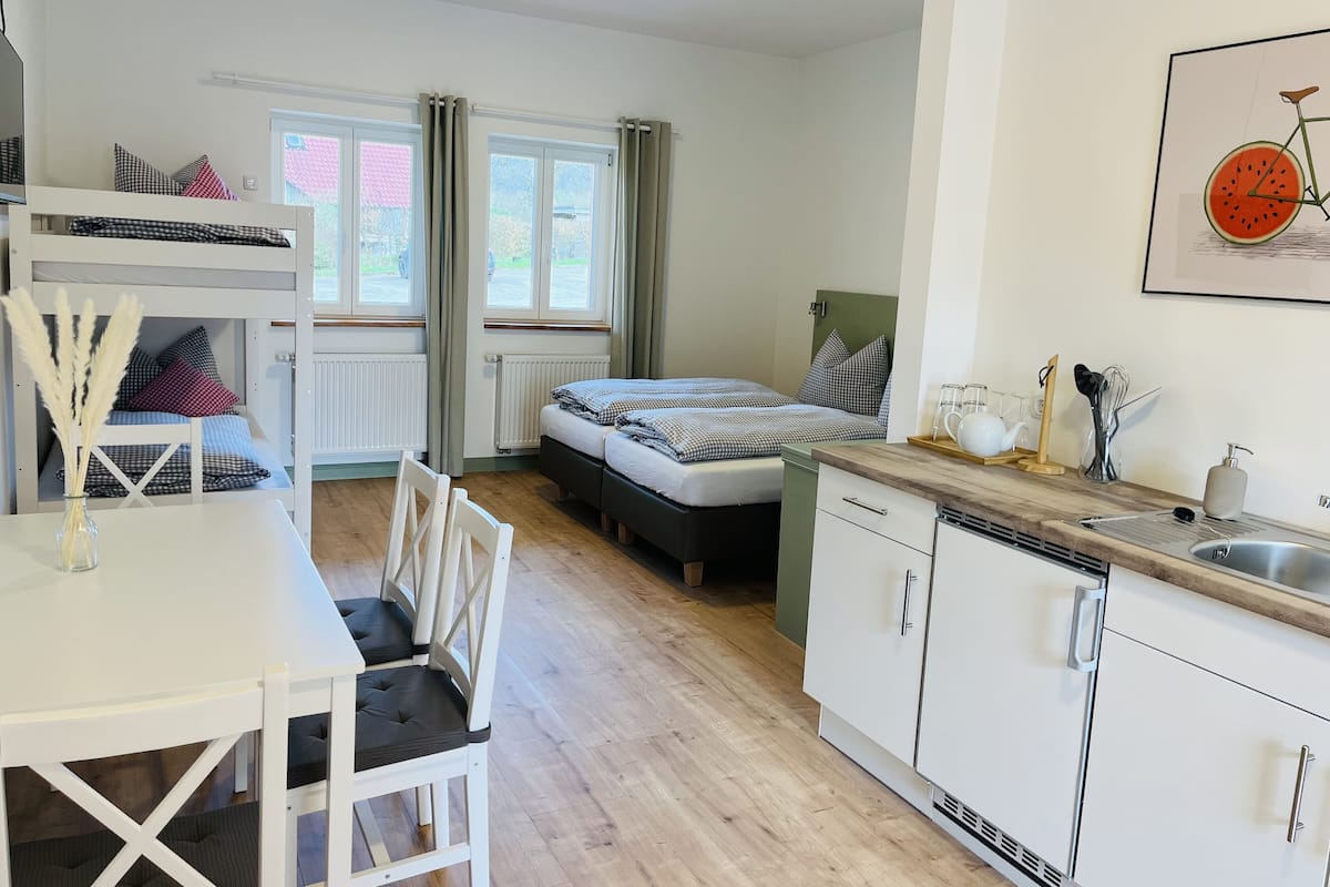 Ein kleines Schlafzimmer mit Etagenbetten, einer kompakten Küchenzeile und einem Essbereich.
