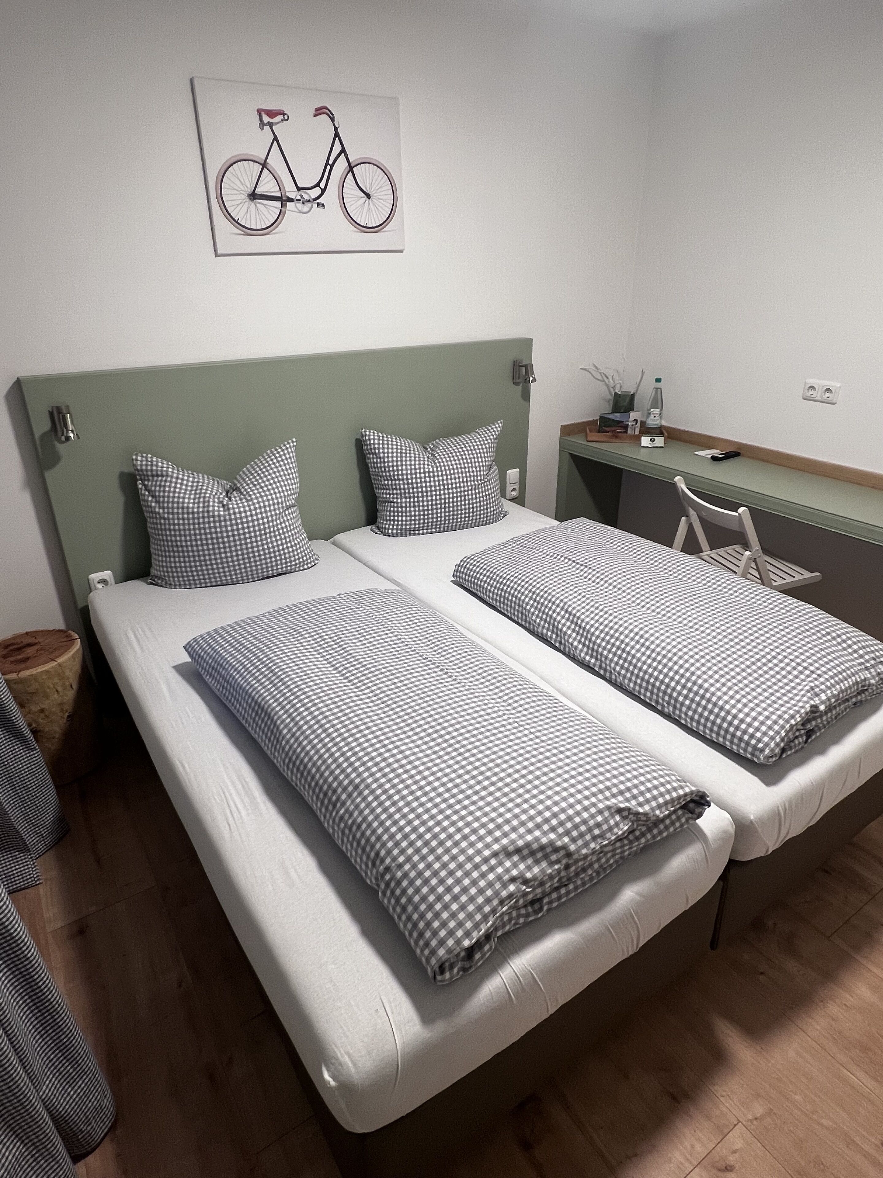 Cama doble con cabecera, dos almohadas, mesita de noche con lámpara y una obra de arte con motivo de bicicleta en la pared.