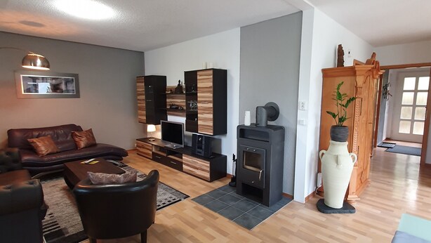 En rummelig stue med sofa, sofabord og TV-møbel. Der er pejs og en stor vase på gulvet.