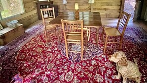 Ein Holzblockhaus-Interieur mit Esstisch, Stühlen, Teppich und einem Hund.