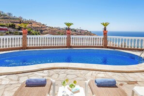 Área da piscina com vista clara do oceano e uma encosta ao fundo.