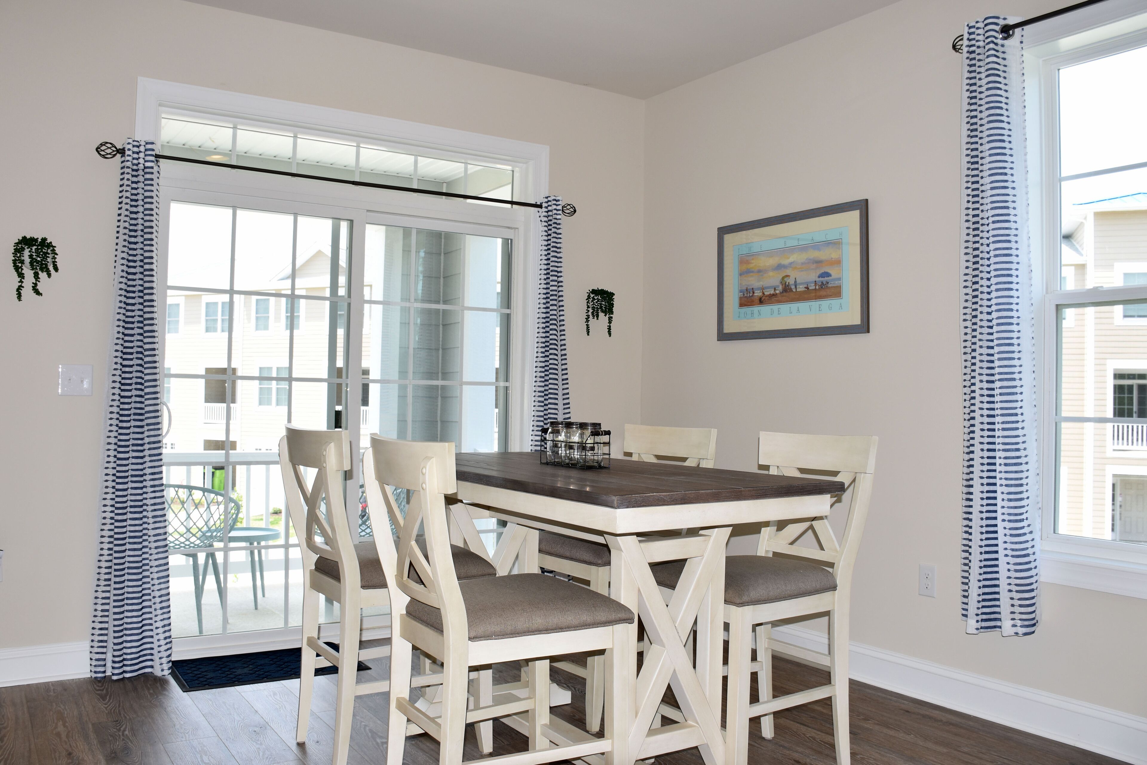 A dining area with a wooden table and chairs, a window with curtains, and a framed picture on the wall.
