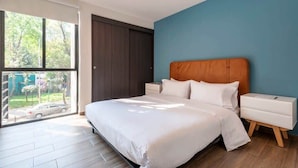 Ein modernes Schlafzimmer mit einem großen Bett, einem Nachttisch, einem Holzkopfende und Blick ins Freie durch ein großes Fenster.