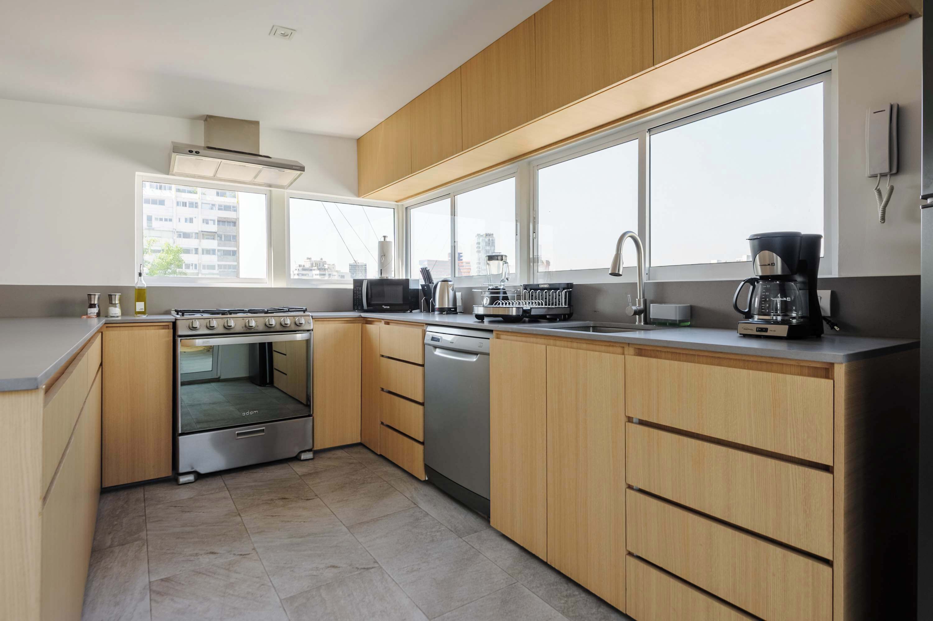 A modern kitchen with a built-in oven, dishwasher, and a large window providing a city view.