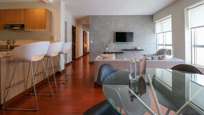 A modern kitchen with wooden cabinets, a dining area with a glass table and chairs, a sofa, and a TV mounted on the wall. - w*| Lush 2BR w/AC Near Kennedy Park in Miraflores (Miraflores)