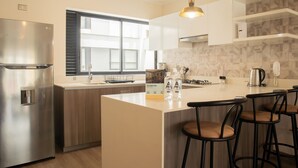 Et moderne køkken med et rustfrit stål køleskab, en stor ø med barstole, en indbygget ovn og en hængende pendel.