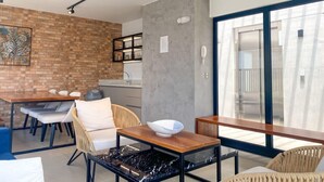 Et moderne køkken med en murstensbagplade, et spiseområde med et træbord og stole, samt en stor skydedør, der fører ud til en balkon.