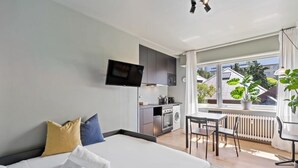 Une chambre d’hôtel moderne dotée d’un grand lit, d’une petite kitchenette, d’un coin repas et offrant une vue sur la ville grâce à de grandes fenêtres.