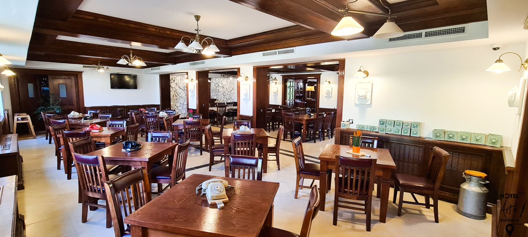 Un restaurante espacioso con mesas y sillas de madera, un teléfono antiguo sobre una mesa, y una pared decorativa con cajas verdes.