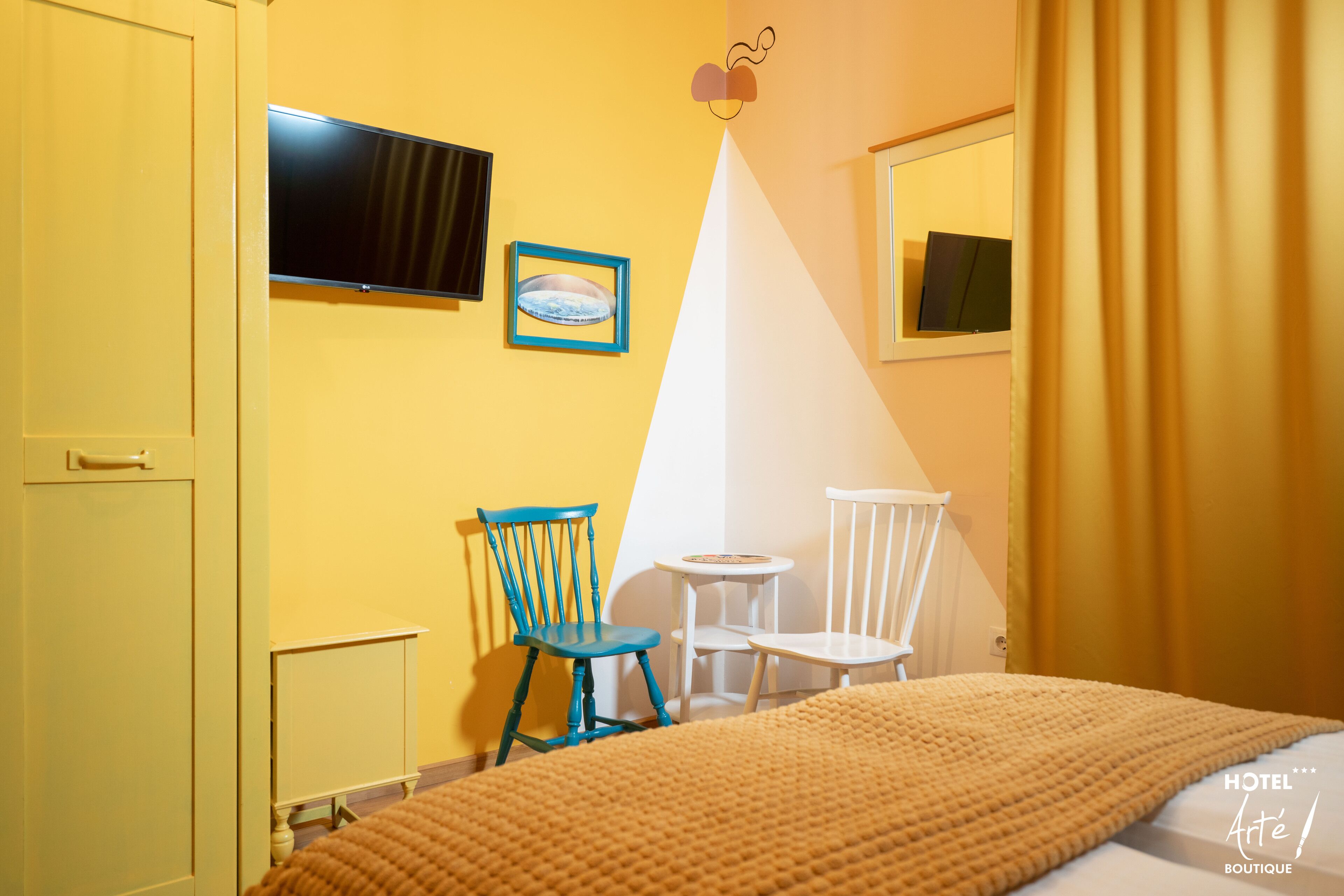 A hotel room with a bed, a television, two chairs, and a small table.