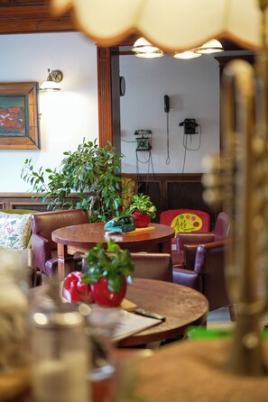 A cozy indoor seating area with wooden tables and chairs, a potted plant, and a wall-mounted telephone.