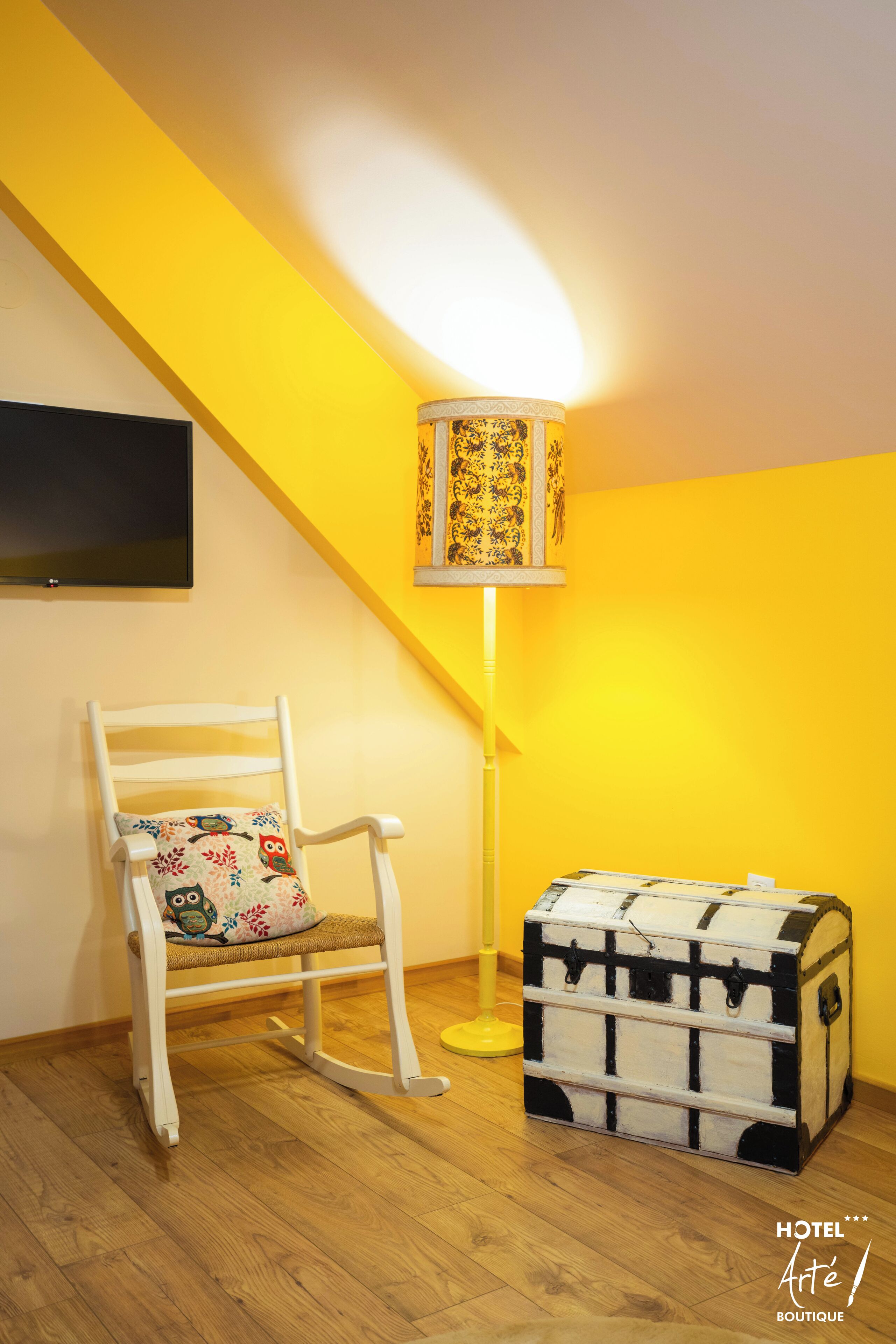 Quarto com uma cadeira de balanço branca, um abajur com padrão e um aparador branco em frente a uma parede amarela.