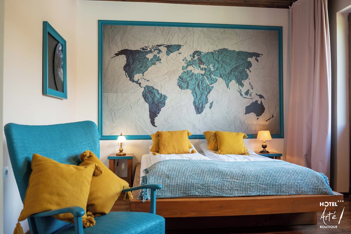 A hotel room with a large world map on the wall, a bed with blue and yellow bedding, and a blue armchair with yellow cushions.