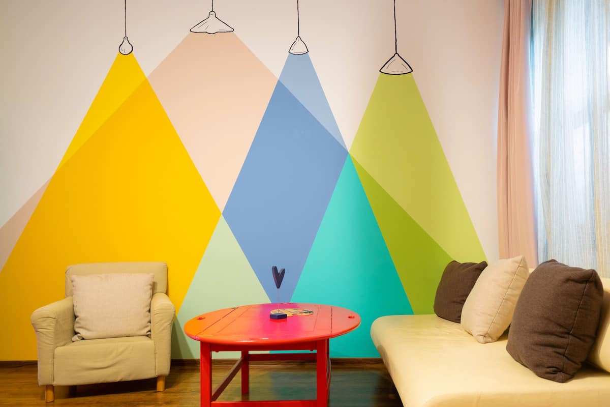 A room with a geometric wall design, a beige sofa, a red table, and a beige armchair.