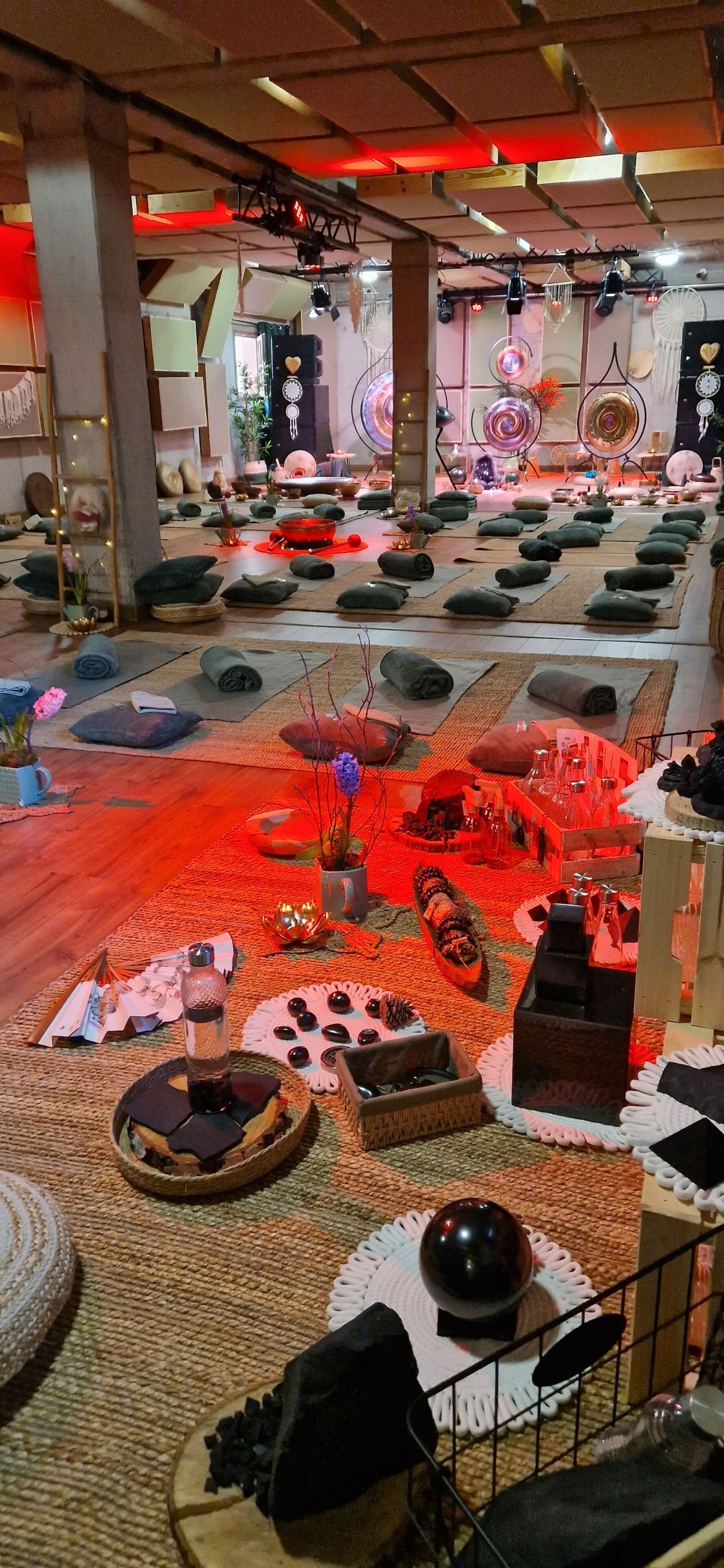 Una habitación con varias colchonetas de yoga dispuestas en filas, distintos objetos decorativos y una zona central con una mesa iluminada con luz roja.