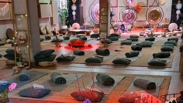 Una habitación con varias colchonetas de yoga dispuestas en filas, distintos objetos decorativos y una zona central con una mesa iluminada con luz roja.