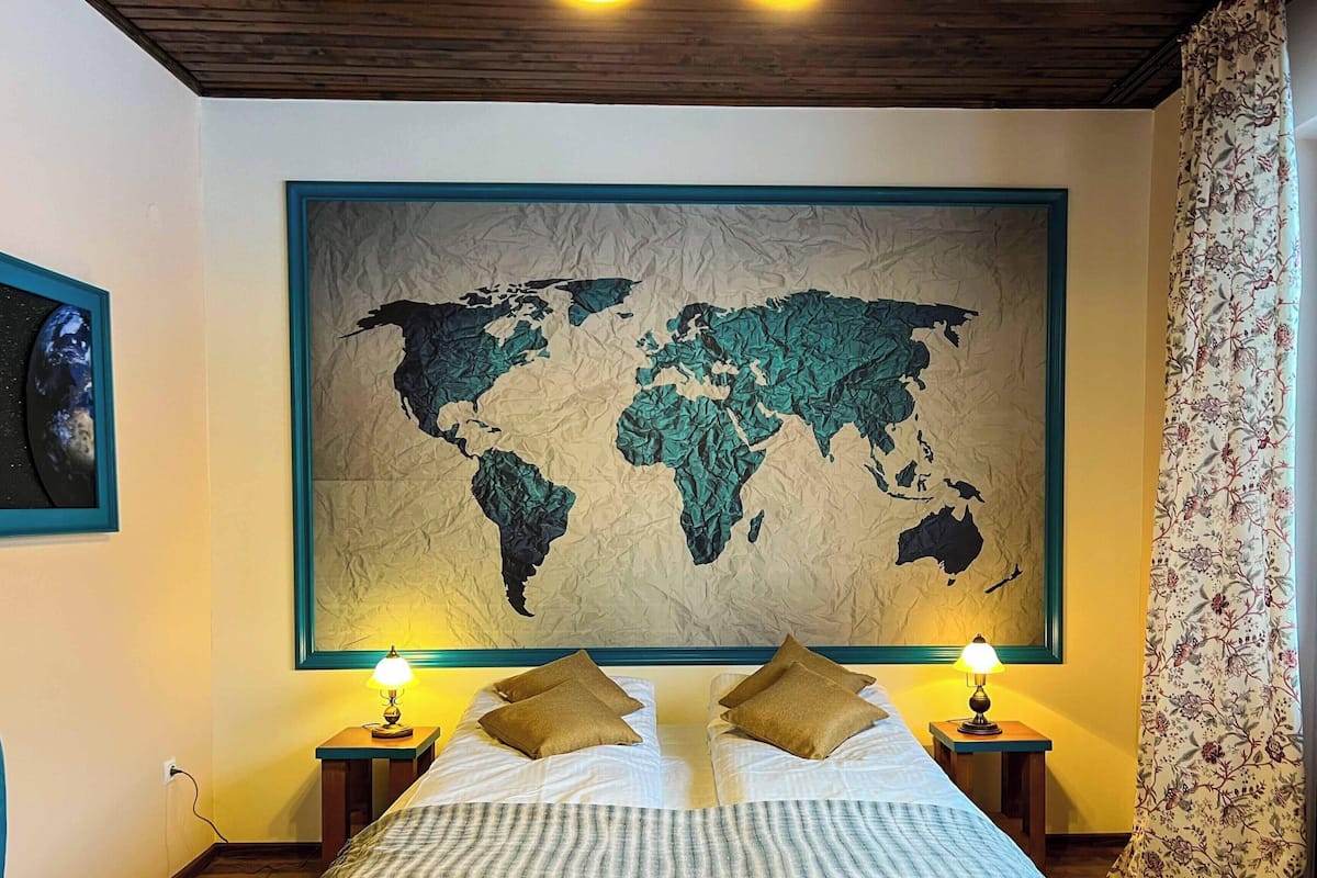 A bedroom with a large world map mural, two bedside lamps, and a bed with pillows.