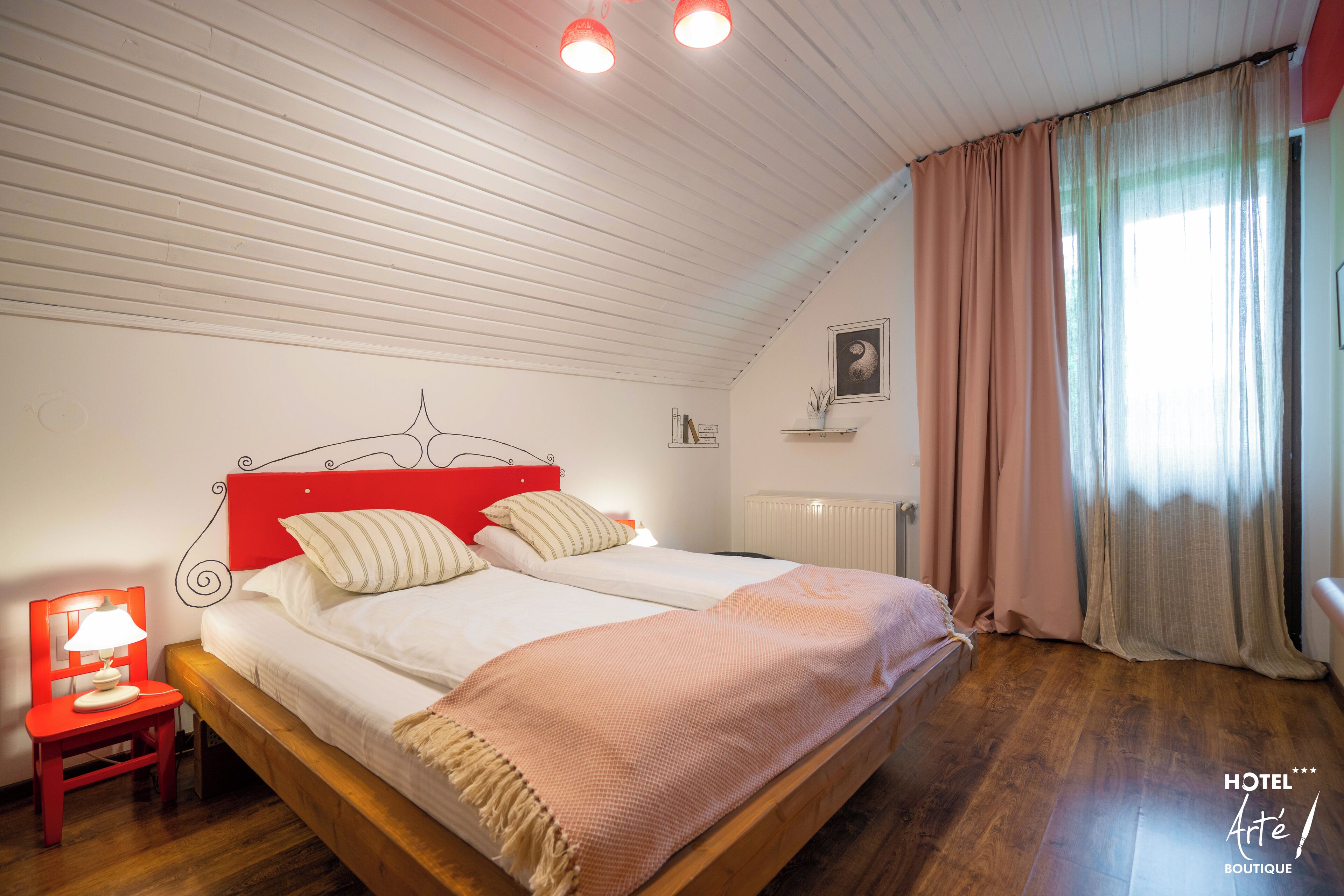 Un dormitorio con cama de madera, cabecera roja, mesita de noche con lámpara y ventana con cortinas.