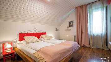 Un dormitorio con cama de madera, cabecera roja, mesita de noche con lámpara y ventana con cortinas.