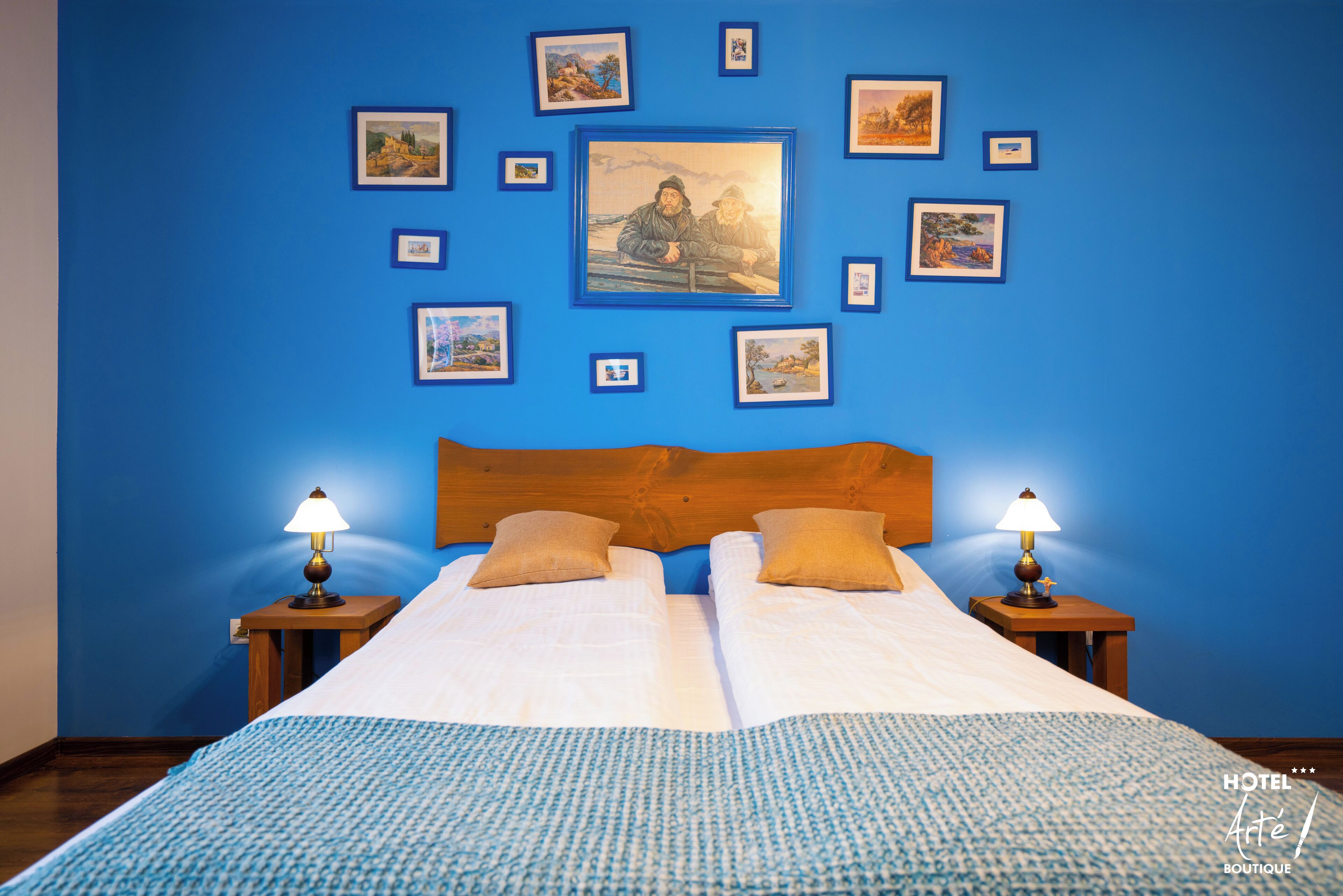 A hotel room with a large bed, two bedside tables with lamps, a wooden headboard, and a wall decorated with framed pictures.
