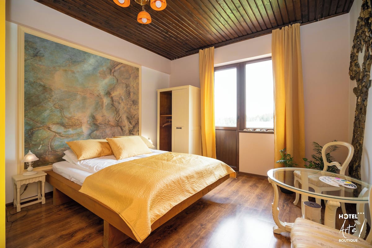 A bedroom with a large bed, a glass table, and a view of the outdoors.