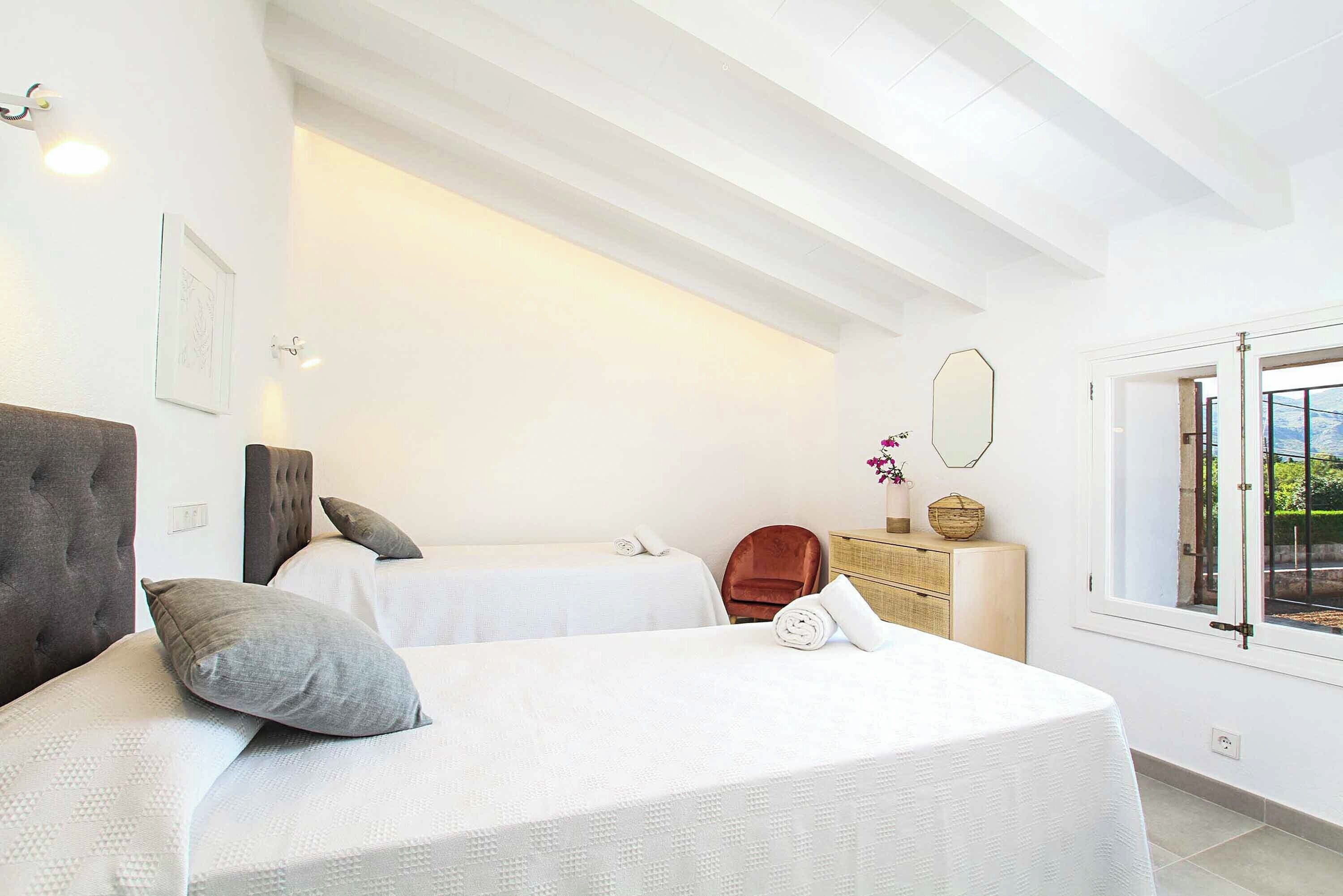 A hotel room with two beds, a wooden dresser, a chair, and a window with a view.