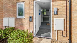 A building entrance with a brick facade, a door, a window, and electrical boxes. - Modern Apartment (Wymondham)