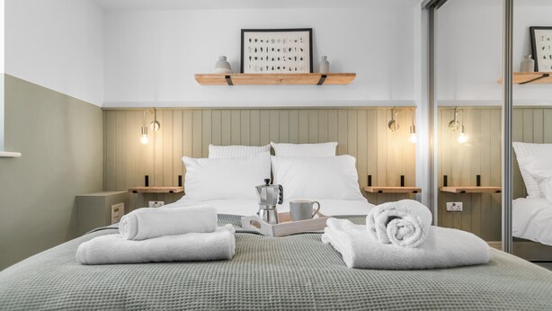 A modern hotel room with a large bed, bedside tables, a coffee maker, and a framed picture on the wall. - Modern Apartment (Wymondham)