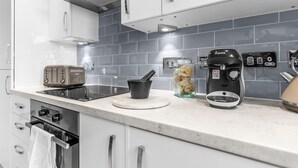 A modern kitchen with a built-in oven, a Bosch coffee maker, and a toaster on the countertop. - Modern Apartment (Wymondham)