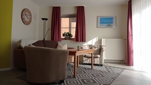 A living room with a sofa, armchair, table, and a clock on the wall.