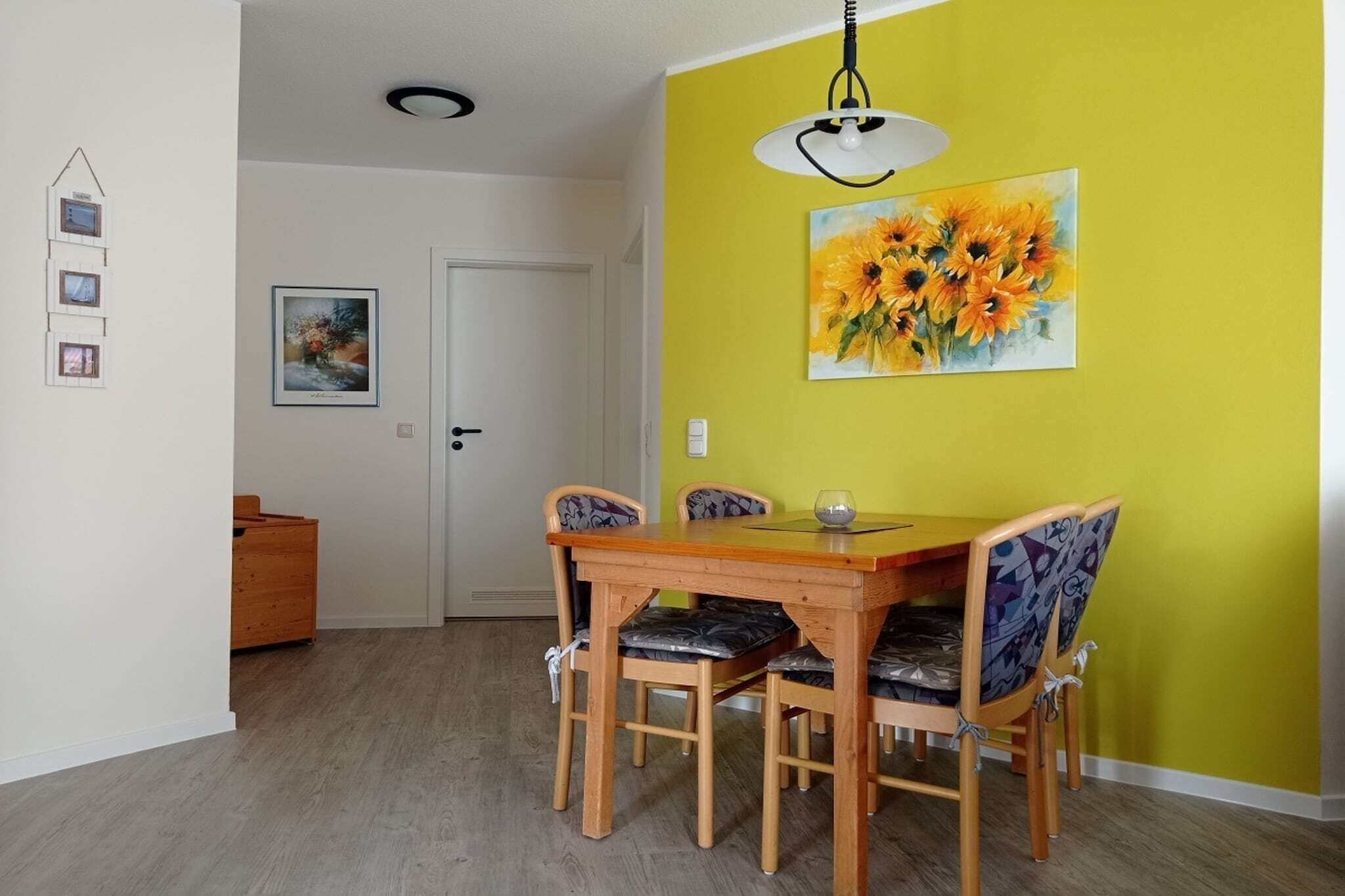 A dining area with a wooden table and chairs, a yellow accent wall, and a sunflower painting.