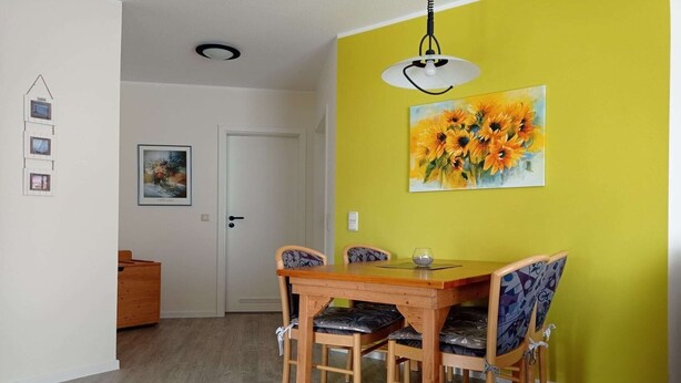 A dining area with a wooden table and chairs, a yellow accent wall, and a sunflower painting.